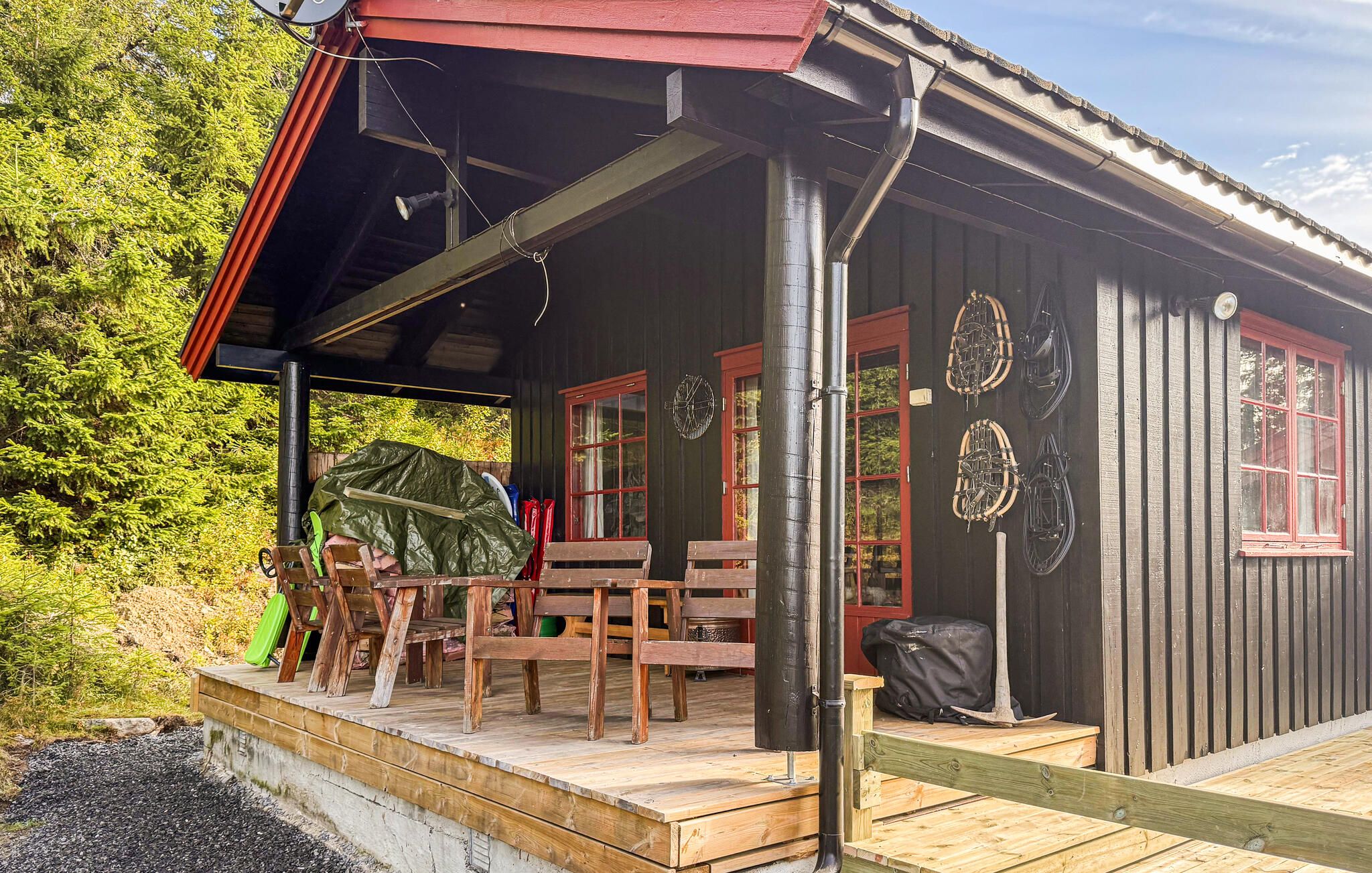 Een houten chalet met een veranda, een rood dak en een metalen schoorsteen.
