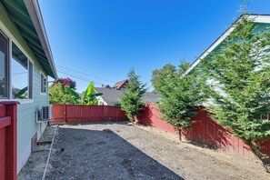 A residential backyard with a red fence, a gravel path, and a house with a green exterior. - Quiet South Tacoma Stay Near Shops, Sound & Parks! (Tacoma)