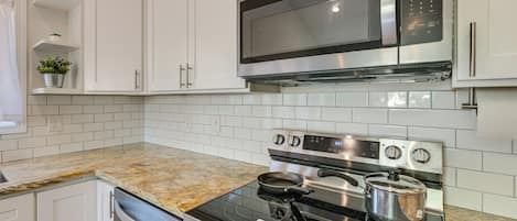 Una cocina moderna con armarios blancos, un microondas de acero inoxidable, un horno y una encimera de granito.