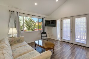 A living room with a sofa, a coffee table, a TV mounted on the wall, and a sliding glass door leading to an outdoor area. - Quiet South Tacoma Stay Near Shops, Sound & Parks! (Tacoma)