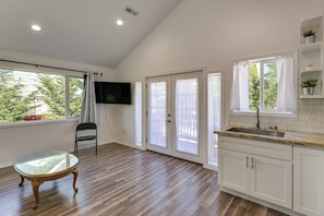 A modern kitchen with a wooden floor, white cabinets, a granite countertop, and a flat-screen TV mounted on the wall. - Quiet South Tacoma Stay Near Shops, Sound & Parks! (Tacoma)