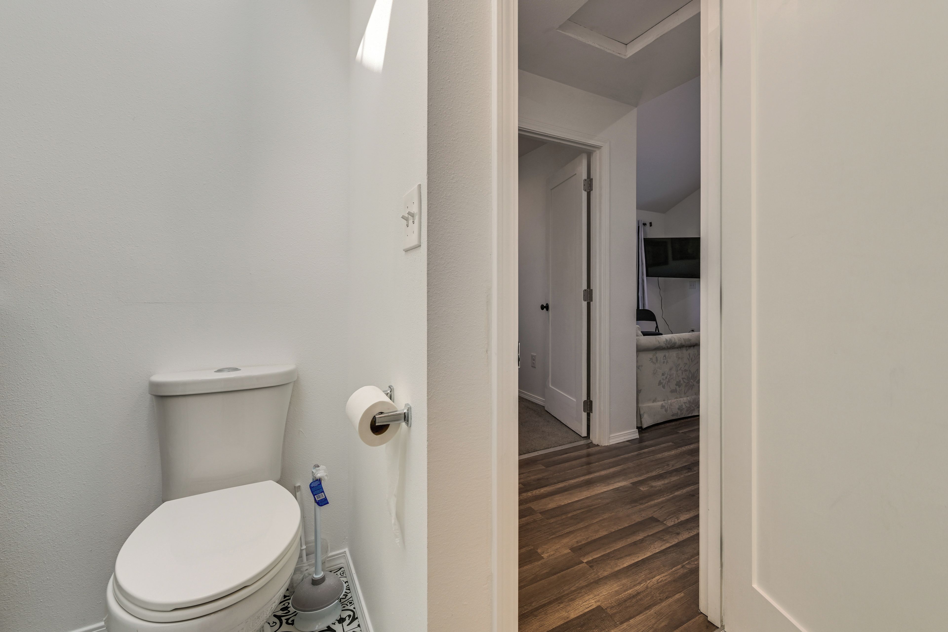 Une salle de bain comprenant des toilettes, un porte-rouleau de papier toilette et un espace douche visible à travers une porte ouverte.