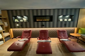 Ein Zimmer mit drei roten Lounge-Sesseln, einem kleinen Tisch und einem an der Wand befestigten Regal mit Dekoration.
