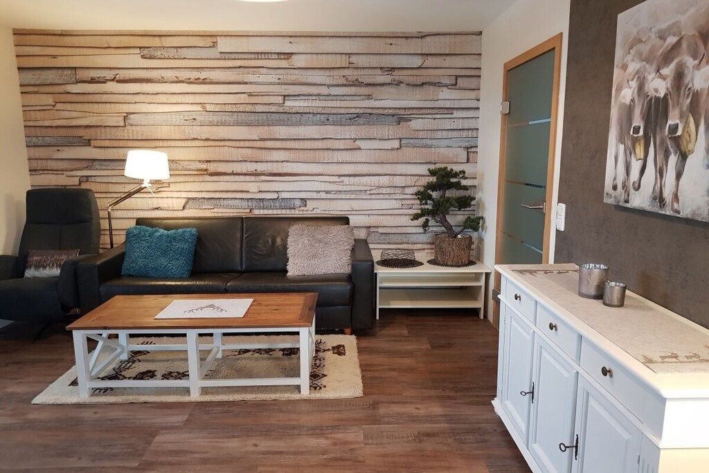 Un salón con panel de pared de madera, un sofá de cuero negro, una mesa de centro, una lámpara y un cuadro de vacas.