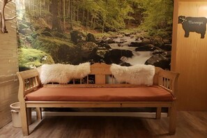 Eine Holzbank mit rotem Kissen und zwei weißen, flauschigen Zierkissen vor einer Wandmalerei eines Waldlaufs.