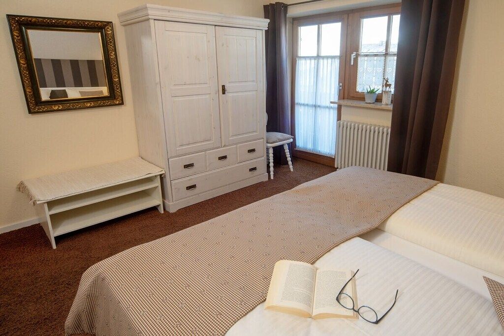 Ein Schlafzimmer mit einem Bett, einem Kleiderschrank, einer Sitzbank, einem Spiegel und einem Fenster mit Vorhängen.