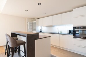 A modern kitchen with white cabinetry, a central island with stools, and built-in appliances. - Villa Alpjuwel-Rubihorn (Oberstdorf)