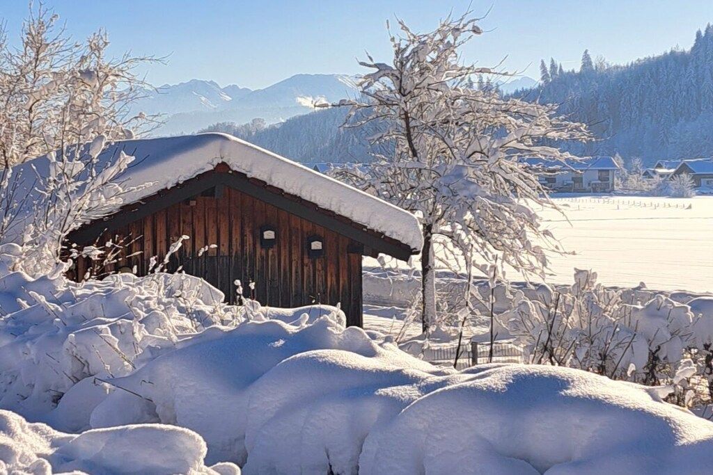 Eine Holzhütte mit schneebedecktem Dach, umgeben von schneelastigen Bäumen und einer Berglandschaft.