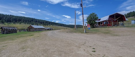 A rural landscape with a dirt road, wooden buildings, and a red barn.