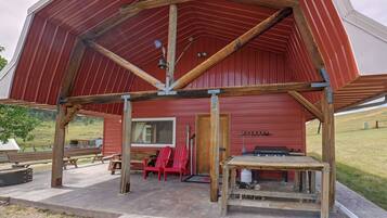Une grange rouge avec une véranda en bois, un banc et une table.