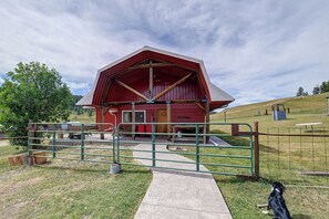 A red barn with a metal gate in front, surrounded by a grassy area and trees.