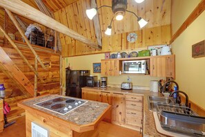 A rustic kitchen with wooden cabinets, a stainless steel refrigerator, a microwave, and a granite countertop.