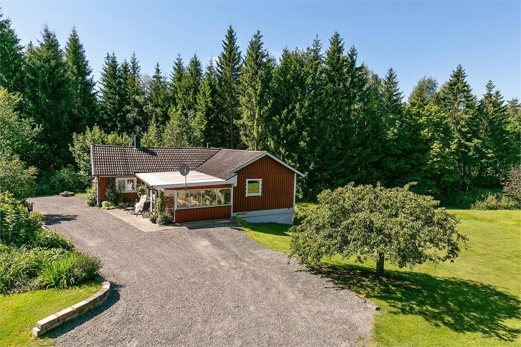 A single-story wooden house with a covered porch, surrounded by a gravel driveway and a well-maintained lawn.