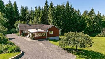 A single-story wooden house with a covered porch, surrounded by a gravel driveway and a well-maintained lawn.