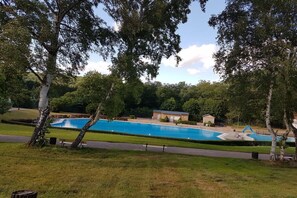 Een zwembad omringd door gras en bomen, met een klein gebouw in de buurt.