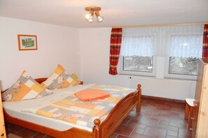 Ein Schlafzimmer mit einem hölzernen Bett, einem fenster mit Vorhängen, einem Heizkörper und einem kleinen Nachttisch.