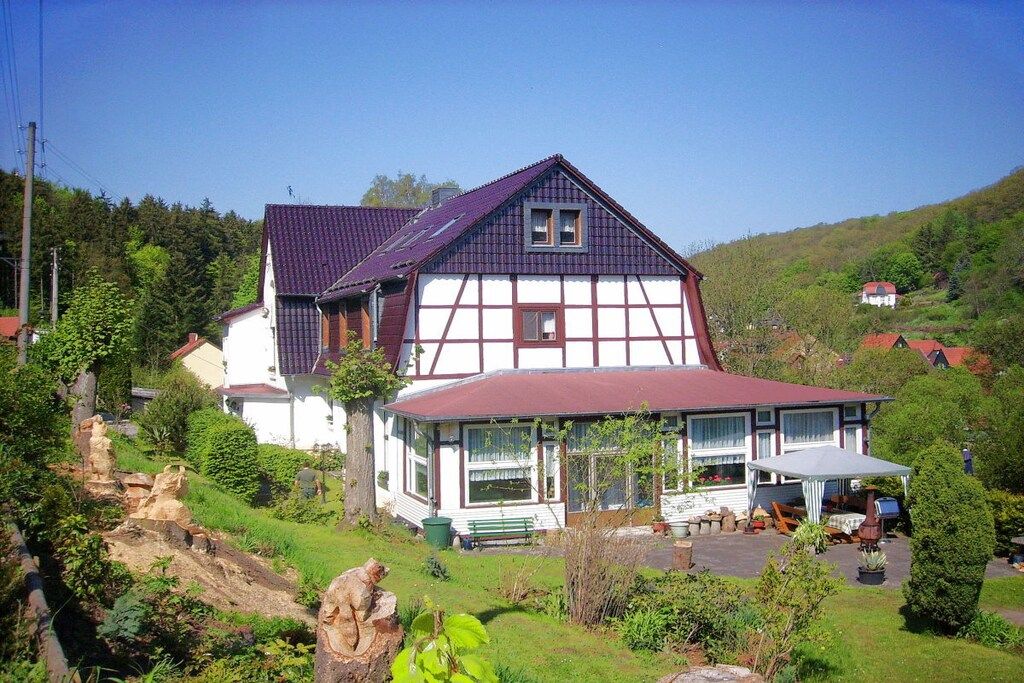 Une maison traditionnelle à colombages, dotée d’un toit en pente, entourée de verdure et de collines.