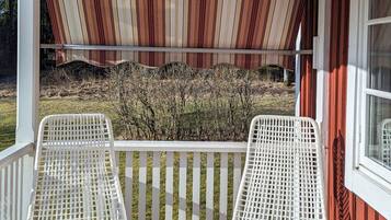 A covered porch with two white wicker chairs and a striped awning.
