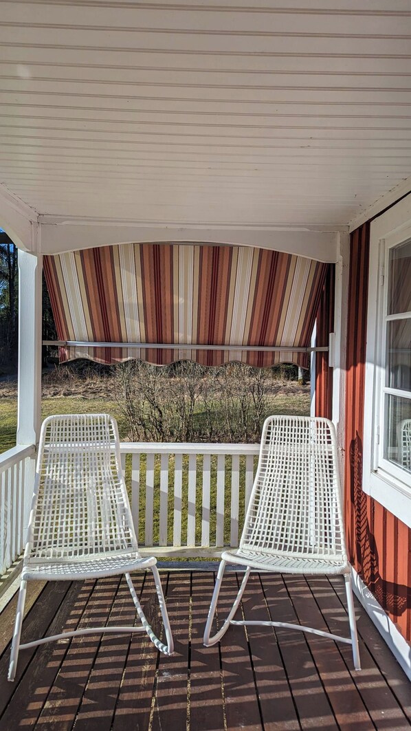 Une véranda couverte avec deux fauteuils en osier blancs et un auvent à rayures.
