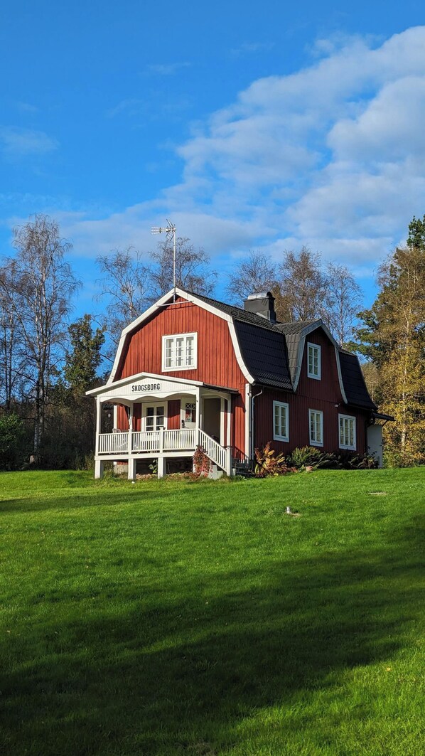 A red wooden house with a white porch and a sign reading 'SKOGSBORG'.