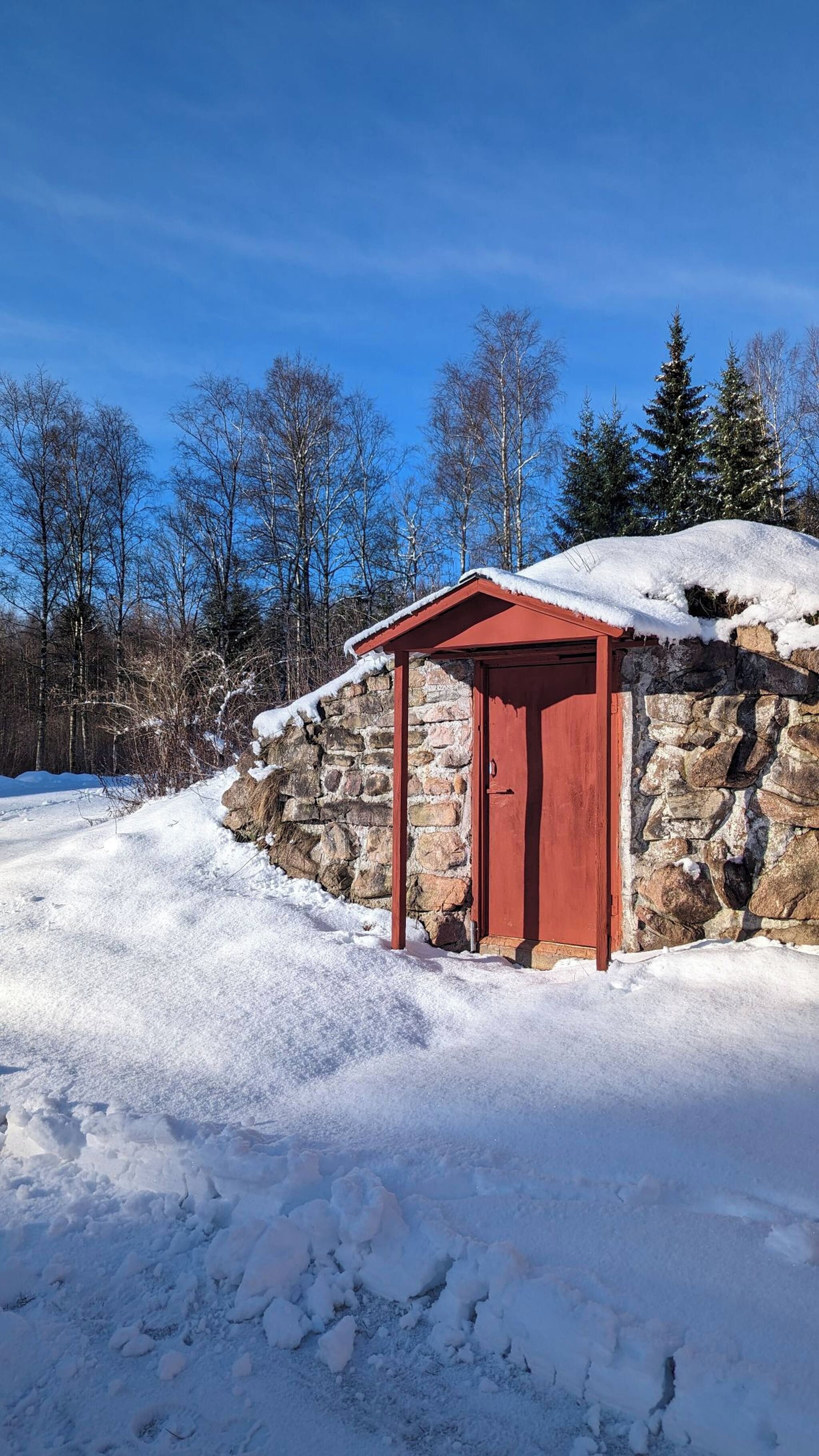 A stone building with a red door and a small overhang.
