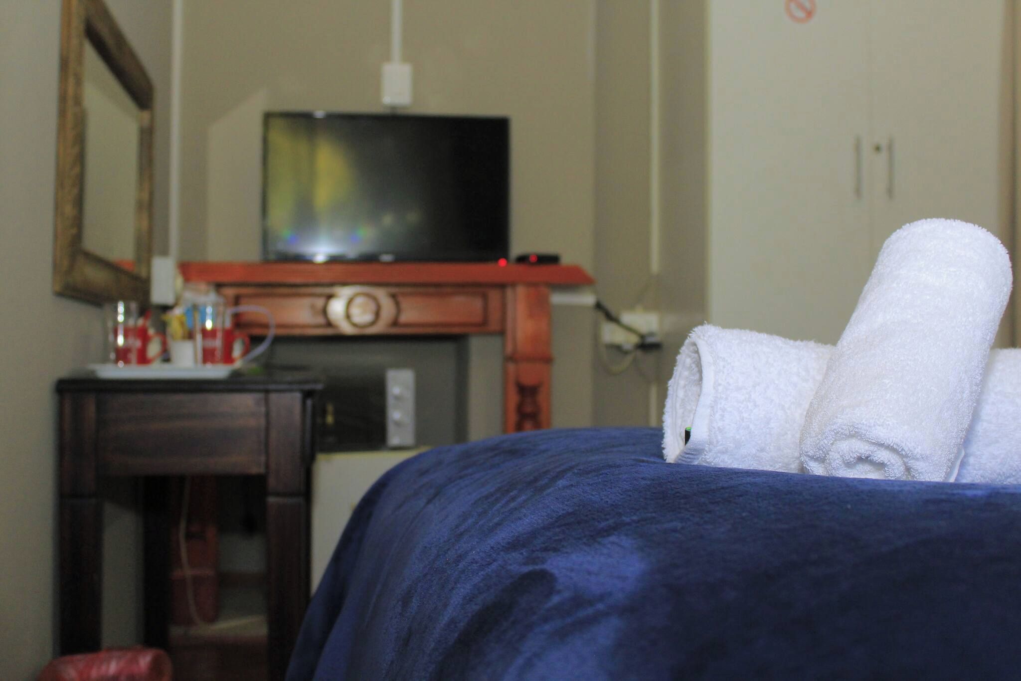 Une chambre d’hôtel avec un lit, un téléviseur posé sur un meuble en bois et une petite table avec une tasse et une bouteille.