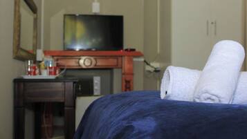 Une chambre d’hôtel avec un lit, un téléviseur posé sur un meuble en bois et une petite table avec une tasse et une bouteille.