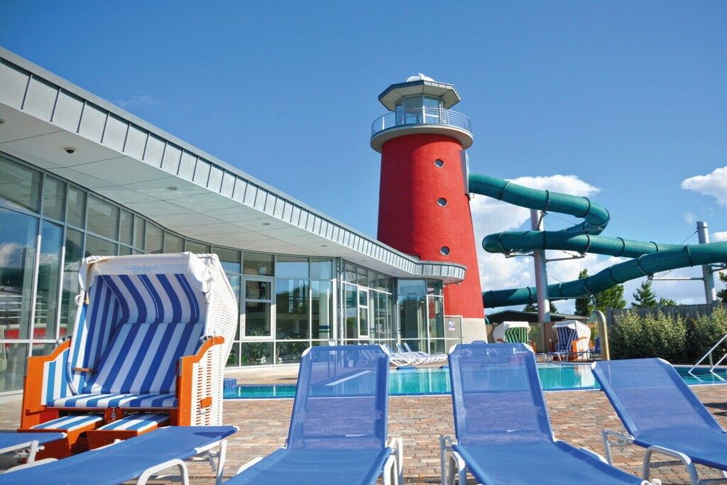 A pool area with lounge chairs, a red lighthouse, and a water slide.