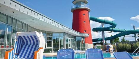 A pool area with lounge chairs, a red lighthouse, and a water slide.