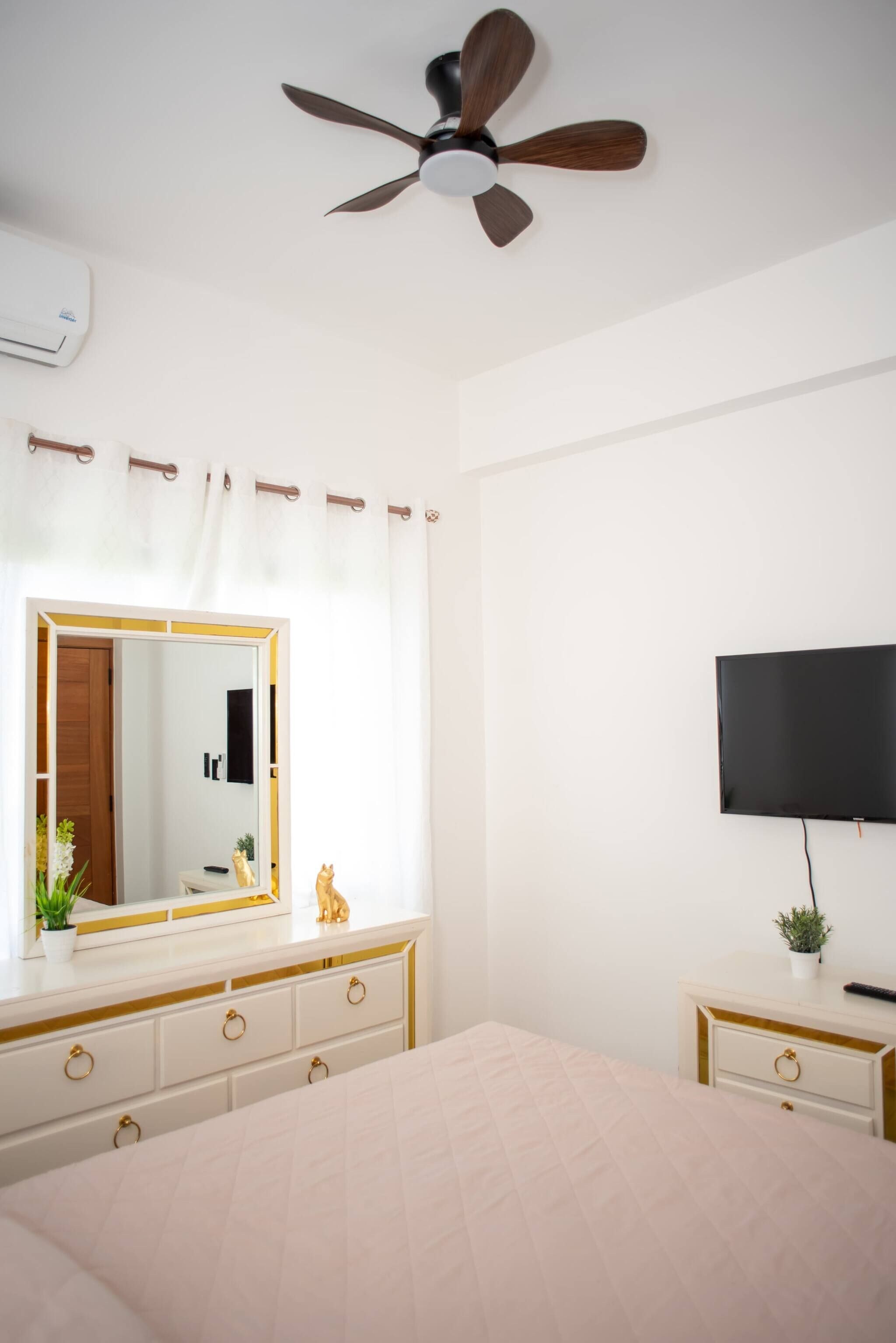 Ein Schlafzimmer mit Bett, Deckenventilator, Fernseher, Kommode und Spiegel.