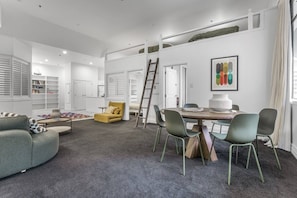 A modern living room with a sofa, a yellow armchair, a dining table with chairs, and a ladder. - Large Waterfront Stay by Britomart & Harbour (Auckland city)