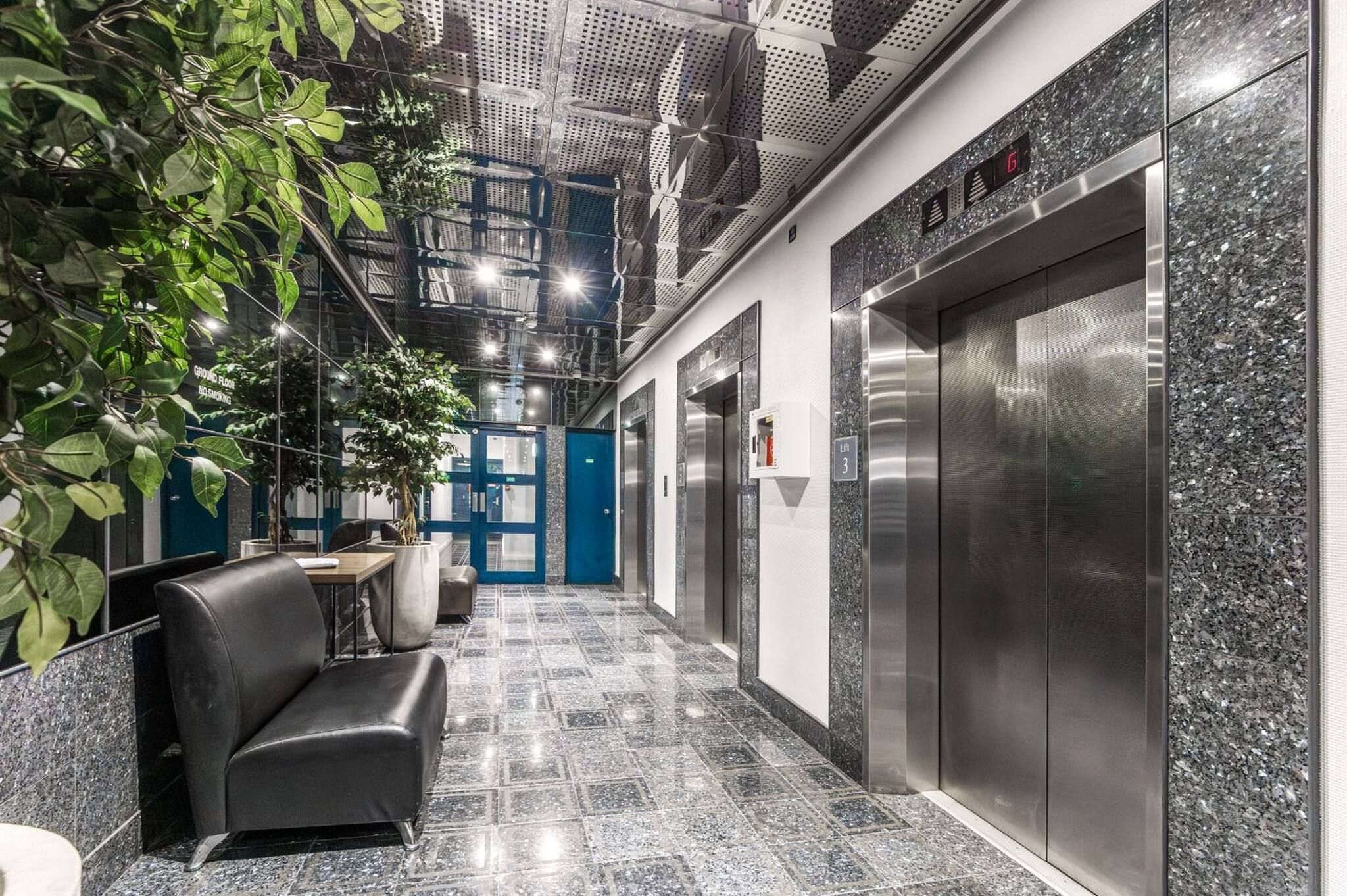 Un espace moderne avec ascenseurs, doté d’un sol en marbre, d’un coin salon avec un canapé et d’un panneau indiquant que le rez-de-chaussée est un espace non-fumeur.