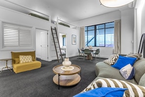 Ein modernes Wohnzimmer mit einer Couch, einem Couchtisch, einem Essbereich mit Stühlen und einer Treppe, die zu einer oberen Ebene führt.