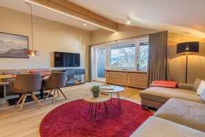 Un salon moderne comprenant un canapé, un coin repas, un téléviseur et une grande fenêtre avec des rideaux.