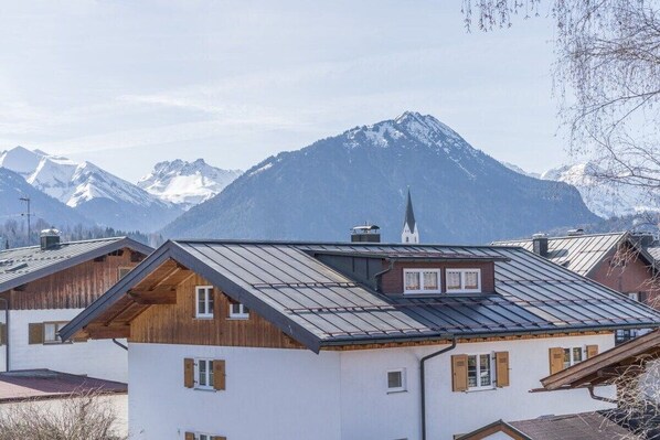 Une cabane de montagne avec un toit en pente, une façade en bois et une vue sur des montagnes enneigées en arrière-plan.