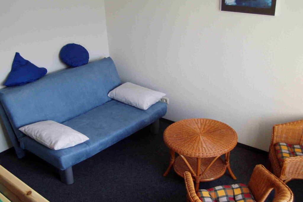 A blue sofa with two pillows, a wicker table, and two wicker chairs in a room with a dark carpet.