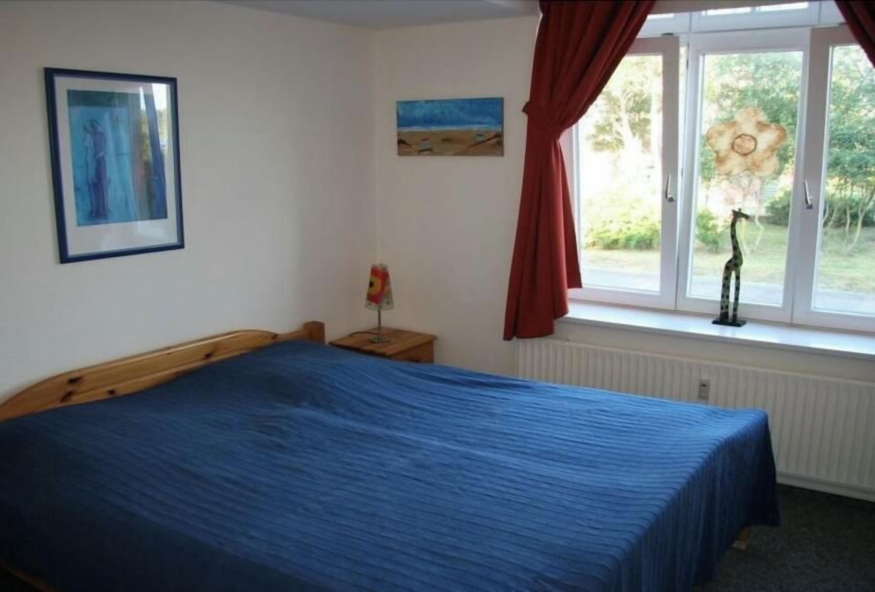 A bedroom with a bed, a nightstand, a window with curtains, and a painting on the wall.