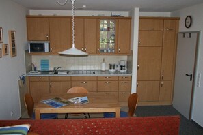 A compact kitchen with wooden cabinets, a microwave, and a dining area with a table and chairs. - Wille in the beach villa Möwennest (Borkum)