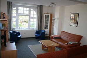 A living room with a brown sofa, blue armchairs, a wooden coffee table, and a window with curtains. - Wille in the beach villa Möwennest (Borkum)