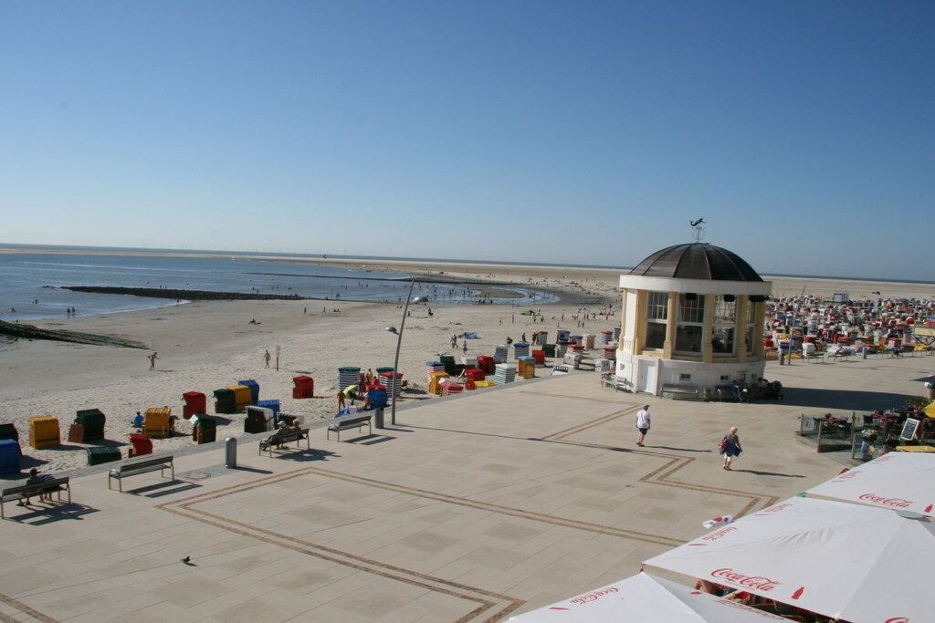 A beach with a pavilion, beach chairs, umbrellas, and a clear sky.