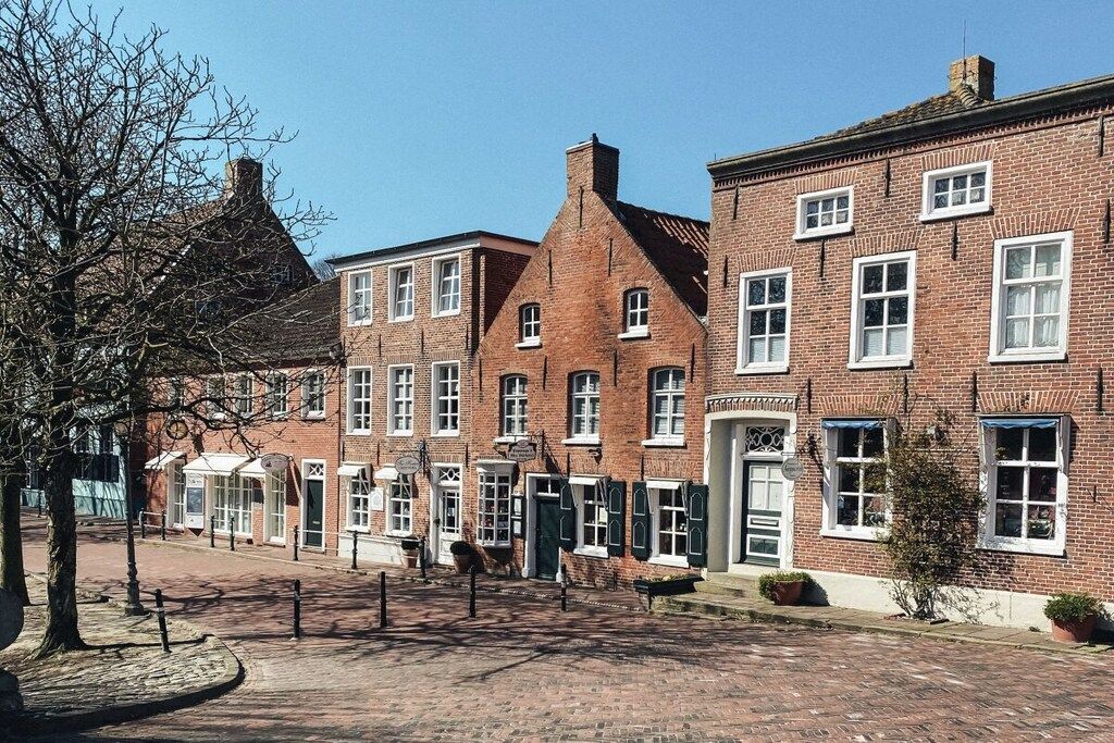 Een rij traditionele bakstenen gebouwen met gelijke ramen en deuren, een geplaveid voetpad en een boom op de voorgrond.