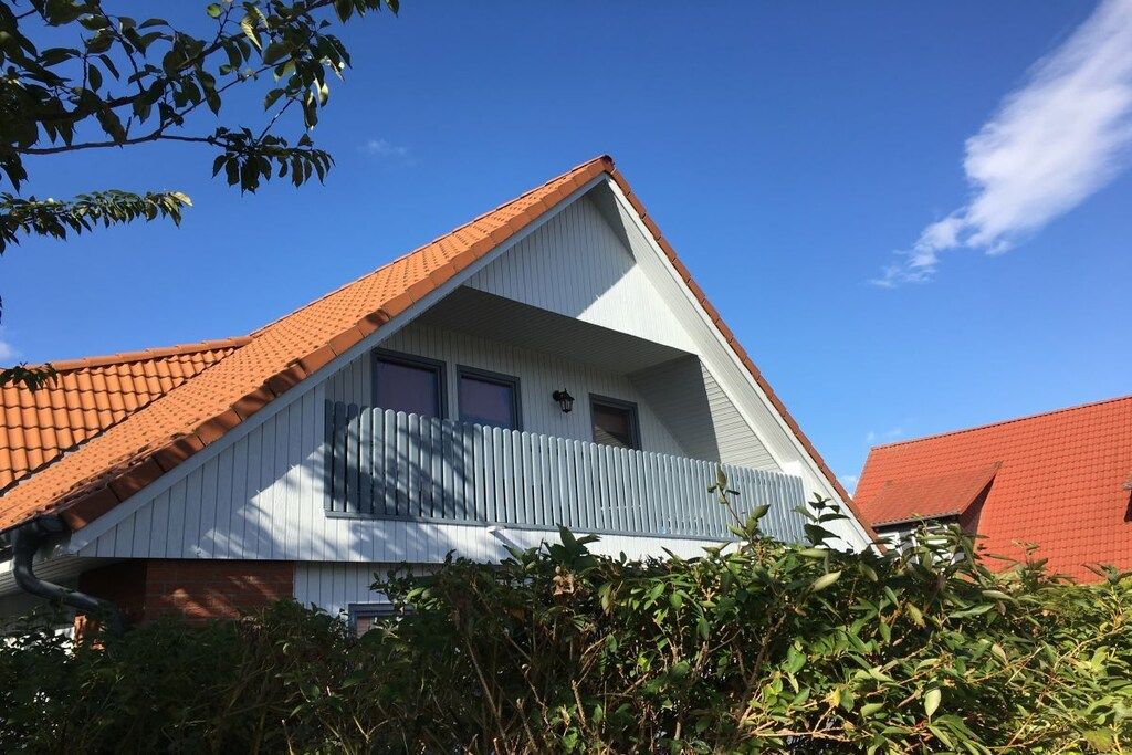 A house with a red-tiled roof, a white facade, and a balcony with a blue railing.