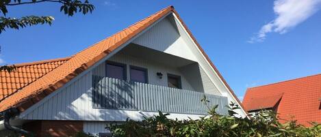 A house with a red-tiled roof, a white facade, and a balcony with a blue railing.