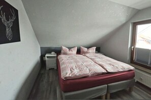 Un dormitorio con techo inclinado, una cama con colchón rojo, dos almohadas, una mesita de noche y una obra de arte en la pared con forma de cabeza de ciervo.