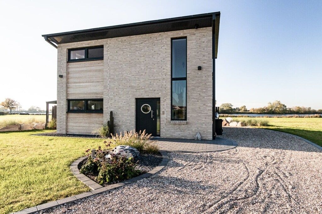 En moderne bygning med to etager, murstensfacade, store vinduer og en grusbelagt indkørsel.
