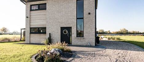 En moderne bygning med to etager, murstensfacade, store vinduer og en grusbelagt indkørsel.