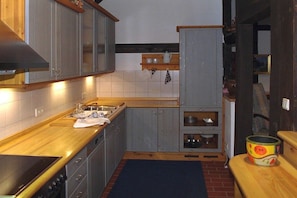 A compact kitchen with grey cabinets, a wooden countertop, a built-in oven, and a small shelf with kitchenware. - Holiday apartment in Trebel with barbecue (Trebel)