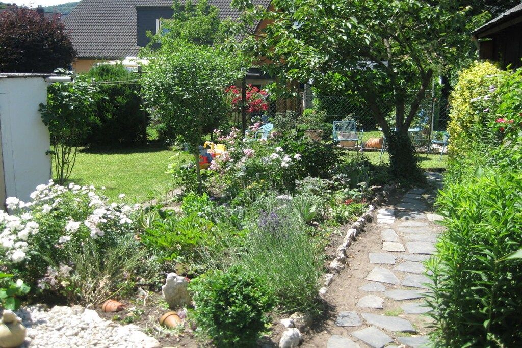 A garden with a stone pathway, various plants, and a small seating area.