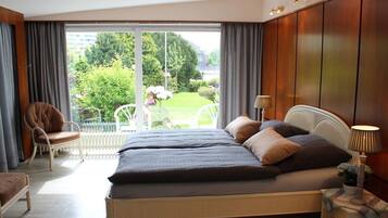 A bedroom with a bed, a chair, a lamp, and a view of a garden through a large window.