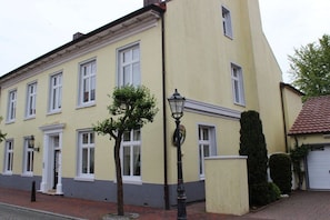 Ein zweistöckiges Gebäude mit gelber Fassade und weißem Zierrat, das mehrere Fenster und einen kleinen Baum vor der Vorderseite aufweist.